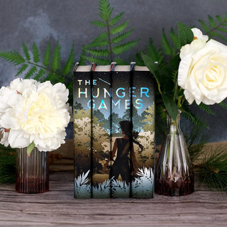 A girl with a bow standing in front of foliage. The Hunger Games limited edition collectible book set featuring custom dust jackets from Juniper Books.