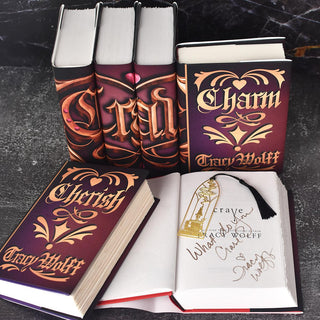 Open book displaying author signature, and laser cut gold bookmark. Open book surrounded by jackets books in series set against a black marble background. 