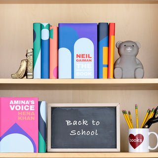 Books Everyone Should Own Young Reader Book Set from Juniper Books sitting on a light wooden shelf surrounded by school supplies.