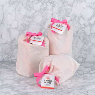 Three Juniper Books neutral canvas gift bags sitting on white marble backdrop with pink ribbon and cards tied on with pink ribbon