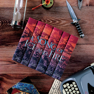 A Song of Ice and Fire sitting on a wood table surrounded by Tolkien's Epic Journey and The Wheel of Time Set from Juniper Books.