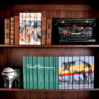 Three Ernest Hemingway Book Set from Juniper Books sitting on bookshelves with antique leather books and a typewriter.