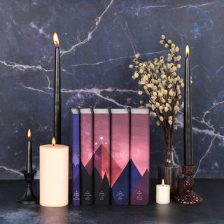 A Court of Thorns and Roses Book Set by Juniper Books set against a black marble black drop surrounded by candles.
