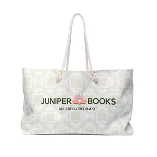 Large canvas light neutral beach bag with white rope handles. Bag fabric is light neutral with white Juniper Books logomark pattern overlay. Juniper Books company name, location, and logo across the side in black..