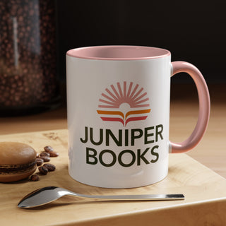 Install of Juniper Books Logo Mug in pink.  Mug sits on wooden cutting board with a spoon, a cookie, and some coffee beans.