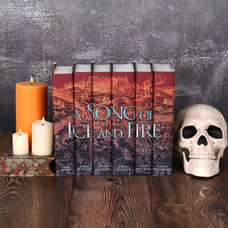 Install shot of A Song of Ice and Fire set from Juniper Books. Set is surrounded by lit candles, antique leather books, and a white skull set against a stone background.