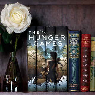 A girl with a bow and arrow standing in front of dense foliage. The Hunger Games custom book set with collectible dust jackets from Juniper Books.