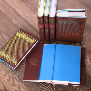 An arrangement of Jane Austen hardcover books with deep red covers and intricate gold foil patterns. Some books are displayed upright, showing their spines. An open book reveals bright blue endpapers and a quote from Jane Austen’s 'Sense and Sensibility' printed in a faux gold font on the inside cover.