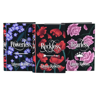 A set of three hardcover books with coordinating dust jackets, each featuring a dark floral design against a black background. The books are titled 'Powerless,' 'Reckless,' and 'Fearless' by Lauren Roberts in white script. 'Powerless' has a design with clusters of purple flowers, 'Reckless' features bold red poppies with an arrow illustration, and 'Fearless' showcases pink roses with a small white crown below the title.