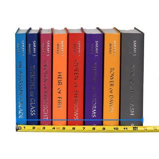 Unjacketed books in the Throne of Glass Series by Sarah J. Maas. Book Spines come in blue, pink, orange, red, purple, yellow, and grey. Title and author name run down spine in silver font, and a tape measure sits against bottom of spines detailing width of complete set.