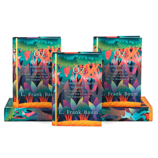 A set of 'The Wizard of Oz' hardcover books displayed with three books standing upright and two lying flat to reveal the colorful cover artwork. Each cover is labeled with the volume number and titles it contains. The covers are decorated with a vibrant forest design in shades of teal, orange, purple, and green, resembling an enchanted woodland. The author, L. Frank Baum, is printed on each cover.