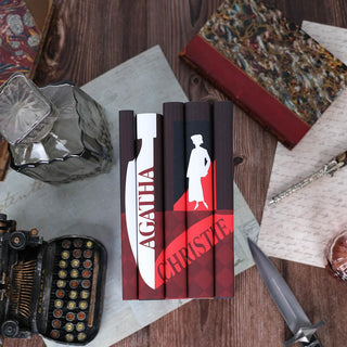 Install shot of Agatha Christie book set set against a wood background surrounded by antique leather books, quill, knife, typewriter, and decanter.