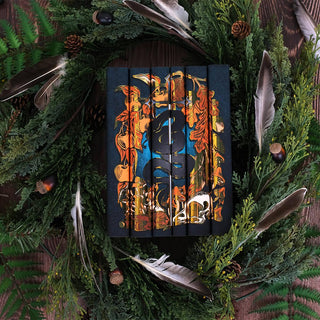 Install shot of The Limited Edition Folk of the Air book set set against wood backgrounded surrounded by greenery, pine cones, and feathers.