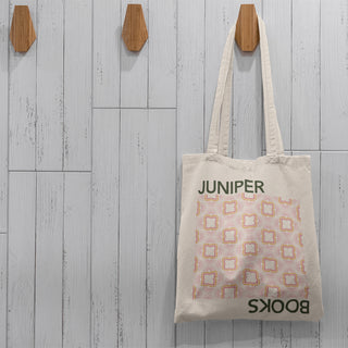 Install of full Juniper Books Tote Bag hung on a wooden hood against a grey wood background.