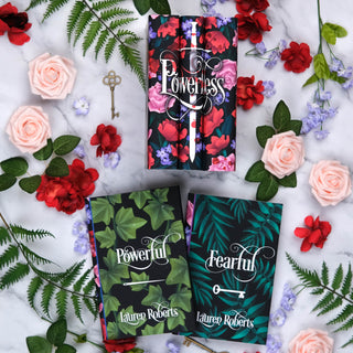 Three books titled 'Powerless', 'Powerful', and 'Fearful' by Lauren Roberts on a marble surface with flowers and leaves designed by Juniper Books.