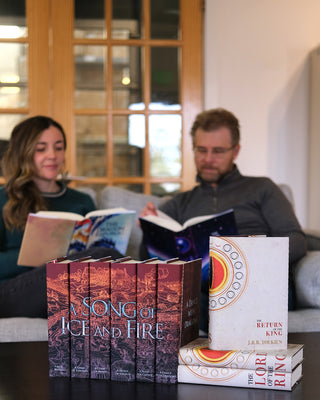 Two people reading books on a couch with 'A Song of Ice and Fire' and 'The Lord of the Rings' books in the foreground.