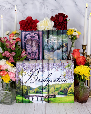 Tiered arrangement of Julia Quinn Bridgerton, Classic Love Stories, and Delicious Solitude Jane Austen Book Sets from Juniper Books surrounded by flowers and candles.