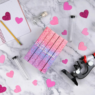 A set of five Ali Hazelwood novels featuring custom book jackets siting on a marble surface surrounded by beakers, a microscope, and a notebook and pencil. Sprinkled through the image there are pink cut-out hearts of various shades.  A continuous design is visible across the spines of all five books, with the name 'Ali Hazelwood' written in white lettering on a pink, blue, and purple gradient background.