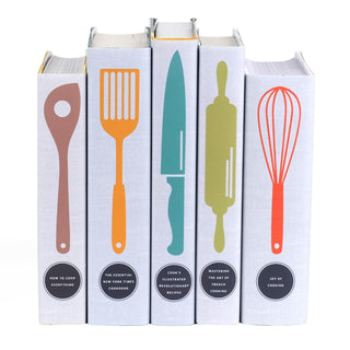 A set of five cookbooks with matching light gray dust jackets, each featuring a minimalist, colorful silhouette of a different kitchen utensil: a wooden spoon, a spatula, a chef’s knife, a rolling pin, and a whisk. The book spines display titles in black circular labels: How to Cook Everything, The Essential New York Times Cookbook, Cook’s Illustrated Revolutionary Recipes, Mastering the Art of French Cooking, and Joy of Cooking.