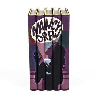 A set of Nancy Drew books featuring modern, artistic dust jackets. The design across the spines forms a cohesive illustration of a silhouetted Nancy Drew holding a flashlight, with her name styled boldly in a speech bubble-like format, creating a sense of mystery and intrigue. The purple, black, and muted tones give the set a contemporary and stylish appeal.