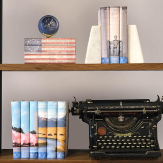 Shelf with the three America 250 book sets from Juinper Books, a typewriter, and decorative items, including a clock and lamp.