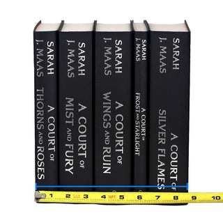 Unjacketed photo of the A Court of Thorns and Roses Series by Sarah J. Maas. Books are black with silver type on the spine detailing book title and author. Tape measure rests against base of spines to show set width.