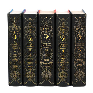 A set of ‘The Wizard of Oz’ books standing upright in a row, each with gold decorative designs and lettering on the spine. The books are titled 'Oz: The Complete Collection' by L. Frank Baum, published by Aladdin. They are labeled Volume 1 through Volume 5, with each volume containing multiple titles from the Oz series, including 'The Wonderful Wizard of Oz,' 'Dorothy and the Wizard in Oz,' 'The Patchwork Girl of Oz,' and others.