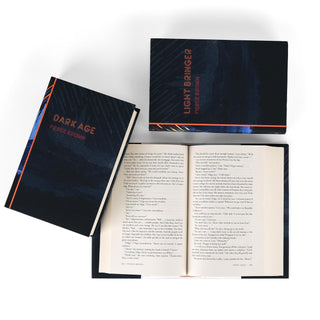 Open book view of Iron Gold, surrounded by Dark Age, and Light Bringer by Pierce Brown. Open book displays print size. The covers feature a dark, mountainous landscape with a minimalistic design copper-colored titles, and the author's name.