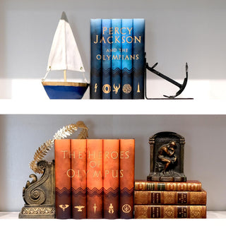 Percy Jackson and the Olympians book set on a white shelf sitting above the Heroes of Olympus book set surrounded by antique books, a sailboat, and an anchor.