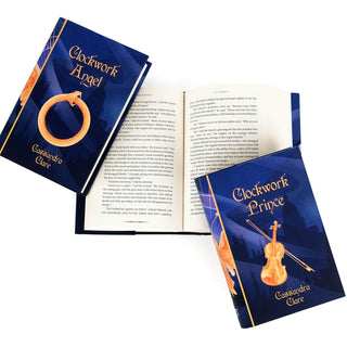 Open book of the Juniper Books Infernal Devices hardcover book set showing an ouroboros and gold violin on each cover.